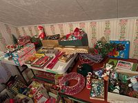 Wide overview of table holding assorted holiday decorations including ornaments, lights, figurines and wrapping supplies