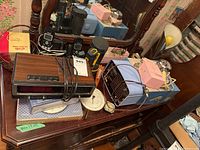 Vintage hair dryers, radios, clocks, phones, and other vintage electronics arranged on a wooden surface. Items include a Westinghouse radio, various clocks and handheld devices.