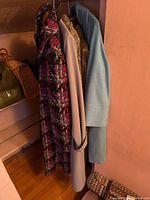 Five vintage ladies' coats hung on a rack, showing variety in colors and materials including a multicolor coat, light blue coat, beige trench, faux leather jacket, and tan jacket.