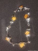 Photo of an 8-inch antique toned sterling silver bracelet with yellow amber flower-shaped accents and silver leaves on a dark background.