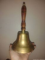Photo of the older brass school bell held in hand showing the wooden handle and brass bell.