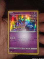 Front side of Deoxys Pokémon card held in hand, showing holographic Fusion Strike Rapid Strike design with attack and HP details.