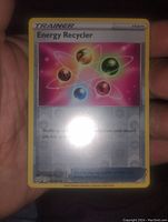 Photo of the Energy Recycler Trainer card held in hand showing reverse holo pattern with colorful energy orb design.