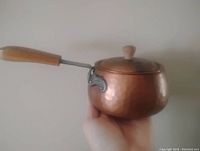 Side view of the hand hammered copper pot held by a hand, showing the wooden handle and glossy copper texture.