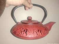 Photo of red cast iron teapot with embossed elephants and bamboo pattern, black handle and lid knob.
