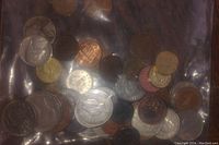 Top-down image showing multiple assorted world coins in a plastic bag, mix of copper and silver toned coins visible.