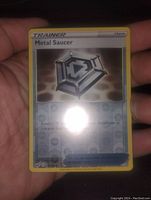 Front view of the Metal Saucer reverse holo Pokemon Trainer card held in hand, showing holo effect and detailed artwork