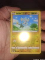 Photo showing a hand holding a Shinx Reverse Holo Pokémon card, displaying the front with holographic background and Pokémon details.