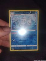 Photo of a Vanilluxe Pokémon card held in hand, showing holographic foil effects with glare, measuring approximately 3.5 inches.