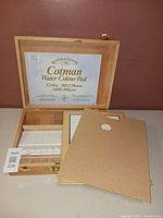 Open wooden artist box with Cotman Water Colour Pad inside lid and painting supplies.