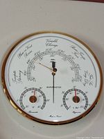 Close-up photo of the barometer face showing center barometric pressure gauge with two smaller dials for temperature and humidity.
