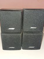 Four small black Bose cube speakers stacked in a 2x2 formation showing front fabric grille with Bose logos.