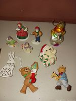 Photo showing multiple assorted Christmas figures and ornaments on a surface, including ceramic figurines, a glass angel ornament, and a decorative rabbit ornament.