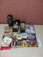 Overview photo showing the Darth Vader tin toy, DVDs, trading cards, graphic novel, dice, and assorted collectibles on table.