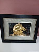 Frontal image of framed Chinese 3D style ship artwork showing gold-tone raised sails on dark background with Chinese characters, housed in black and silver textured frame.