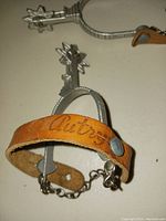 Top view of one metal toy cowboy spur showing star-shaped rowel, metal body, and brown leather strap with embossed 'Autry'.
