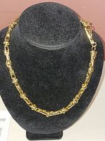 Gold tone costume necklace displayed on a black necklace stand showing front view of the chain design.