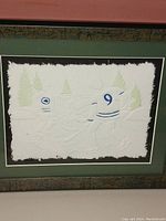 Framed cast paper hockey artwork with two players numbered 5 and 9 skating in front of pine trees, showing textured detail and rough paper edges.