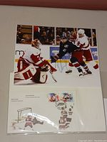 Photo showing the Canada Post first day postcard featuring hockey stamps and a protective plastic sleeve containing the card with postmark along with signed hockey action photograph.