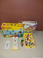 Photo showing LEGO Classic 11008 box, LEGO Disney Belle Adventure 43177 box and pieces, and two LEGO-themed erasers or stands in packaging.
