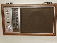 Front full view of vintage Realistic MTA-12 AM/FM radio showing wooden walnut grain case, large speaker grille, and metallic tuning/controls panel