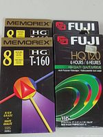 Four sealed blank VHS tapes: two Memorex HG T-160 (8 hours) and two Fuji HQ120 (6 hours), front view showing branding and packaging.