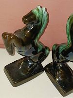 Pair of vintage ceramic horse figures in green and brown glaze, shown side by side from an angled side view to highlight the rearing pose and base.