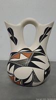 Front view showing double spout, curved handle, and geometric black and terracotta designs on off-white surface.