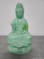 Front view of the Chinese Kwan Yin sculpture made from pale green jadeite resin, showing detailed facial features, lotus pedestal, and branch in hand.