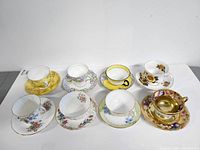 Photo of the 8 teacup and saucer sets arranged in two rows showing all cup and saucer pairs and their decorative patterns.