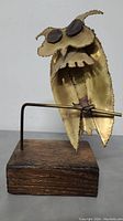 Front view of copper owl sculpture showing detailed textured edges and large copper eyes mounted on wooden base