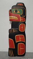 Front view of the hand-carved bear totem pole plaque showing the intricate traditional colored painting in black, red, yellow and green.