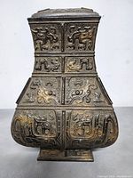 Front view showing detailed dragon and mythical creature relief on square bronze vase with patina and gold highlights.