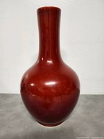 Front view of the copper red glazed vase showing its rounded body and tall neck.