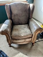 Front view of the all leather reclining chair showing the wingback design, textured brown leather upholstery, nailhead trim on armrests, and cushioned seat.