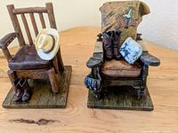 Two custom stone figurines depicting rustic western chairs with cowboy hats and boots, positioned on a wooden base.