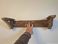 Front view of the rustic wooden wall shelf mounted on wall, showing natural wood texture with branch supports.