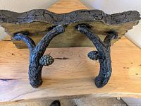 Underside view showing two naturalistic wood branch supports with carved pinecone details attached to the rectangular shelf