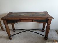 Hardwood coffee table with decorative tile and leather inlays on tabletop, visible turned legs and metal cross-bracing base