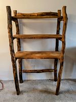 Full front view of the handmade wooden shelf unit showing the raw wood legs and four shelves.