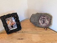Fox portrait in a detailed black textured frame and wolf portrait on stone-like plaque with paw prints and text.