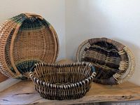 Three custom woven wicker baskets in various shapes and natural color patterns placed on wooden surface against wall.