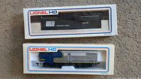 Two Lionel HO scale locomotives still in original boxes, one Penn Central black model 6700, one Santa Fe blue and silver locomotive.