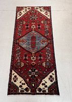 Full view of rug laid flat showing red field with central blue medallion and ivory spandrels