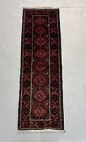 Full view of rectangular Persian Baluchi hand knotted runner rug with red and black geometric patterns on light background
