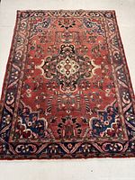 Full view of rug on floor showing red field, border and overall design.