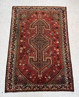 Full view of red and grey Persian Shiraz rug depicting geometric central medallion and detailed border designs on concrete floor