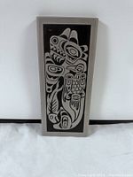 Front view of rectangular aluminum plaque with black background and silver formline design depicting Whale and Raven.
