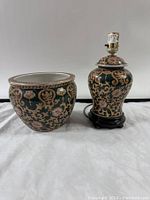 Front view of matching lamp and pot showing ornate floral and scroll design in gold and pink on green ceramic.