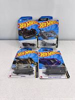 Photo showing four Batman themed Hot Wheels cars in original packaging arranged on a white surface.